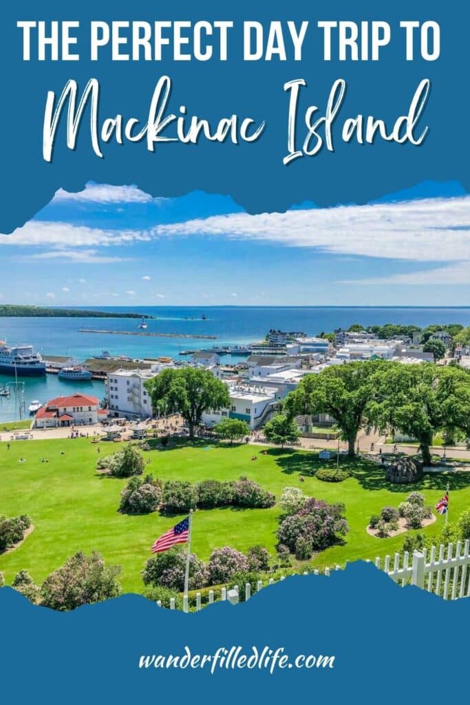 Photo with text overlay. The photo is looking out over a small downtown with a green grassy park nearby and water with a dock on the other side. Text overlay reads A Perfect Day Trip to Mackinac Island.