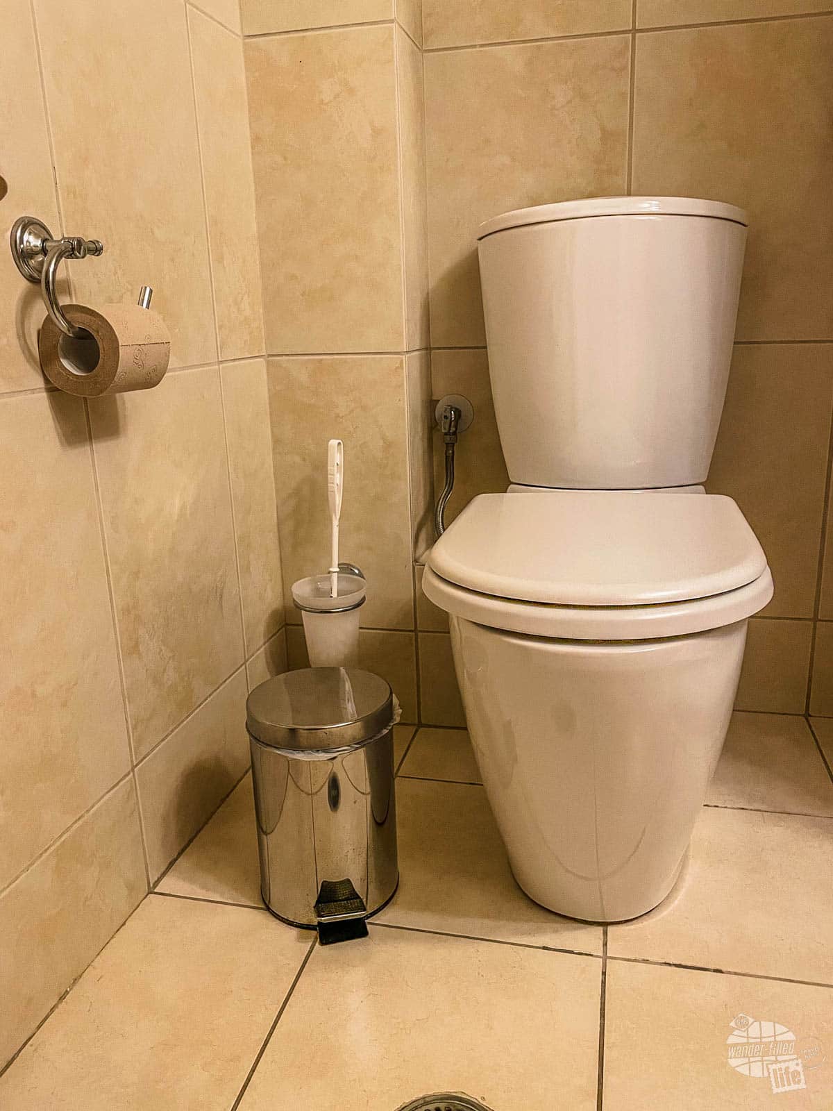 A toilet in Greece with a trash can beside it.