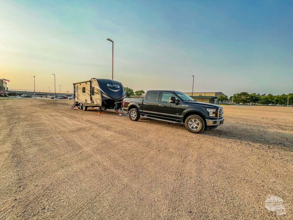 A black F-150 and towable RV camping in a large open gravel lot. 