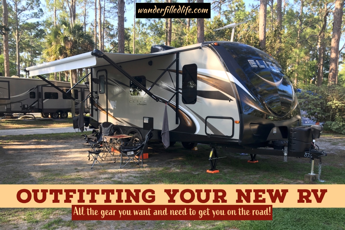 Photo with text overlay. The picture shows a travel trailer at a campsite with camp chairs and a folding table set up in front. Text reads Outfitting Your New RV, All the gear you want and need.