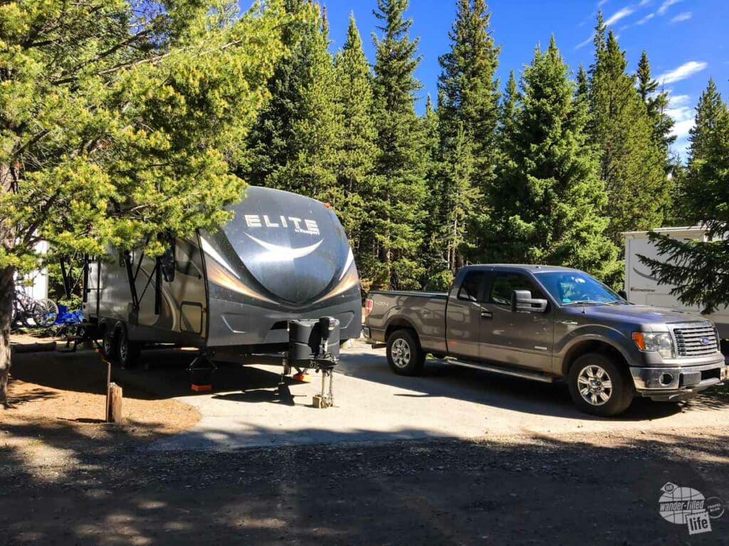 A travel trailer in a campground surrounded by trees.