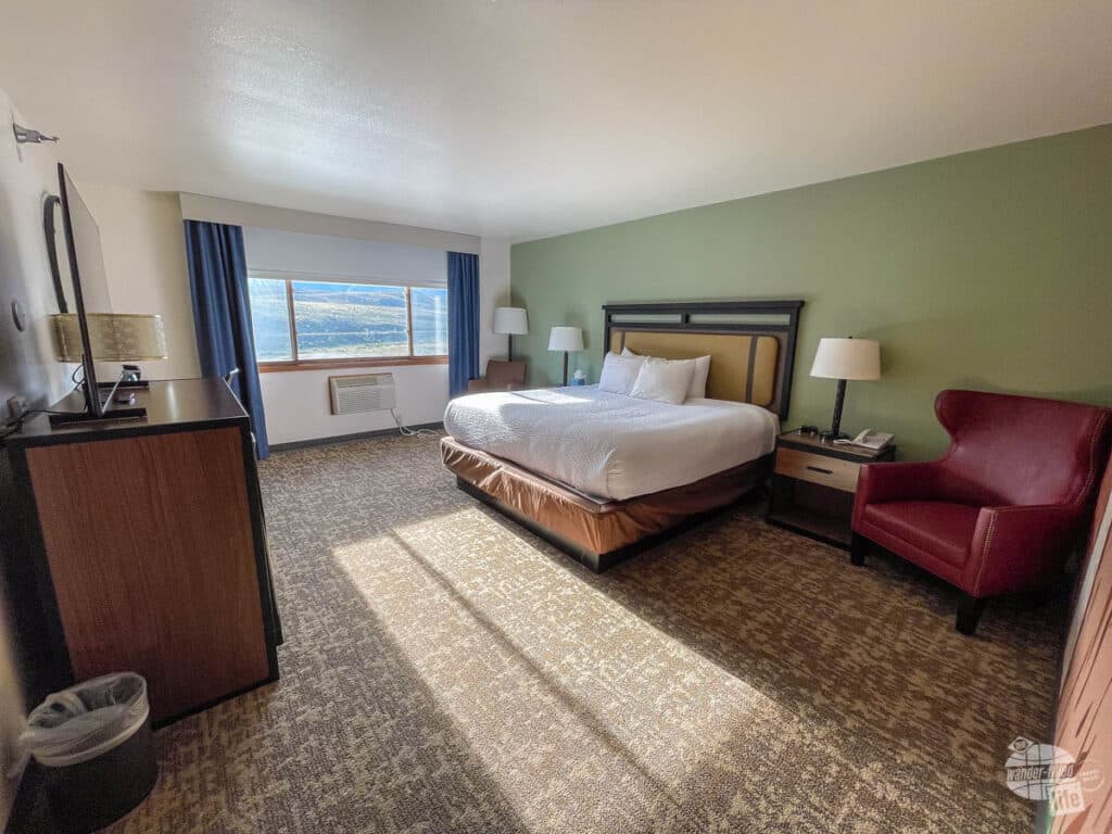 A hotel room with a king bed and a large picture window. 