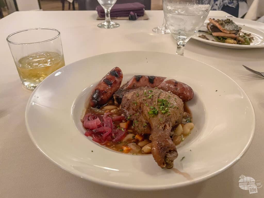 A dinner plate filled with sausage, duck confit and beans.