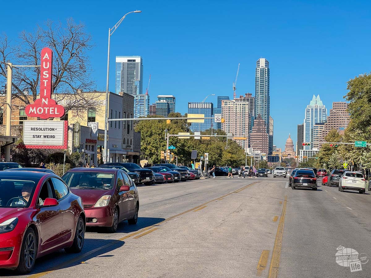 A wide street lined with businesses and tall buildings of downtown in the background. This is along South Congress Avenue in Austin, one of the stops on this Texas road trip.