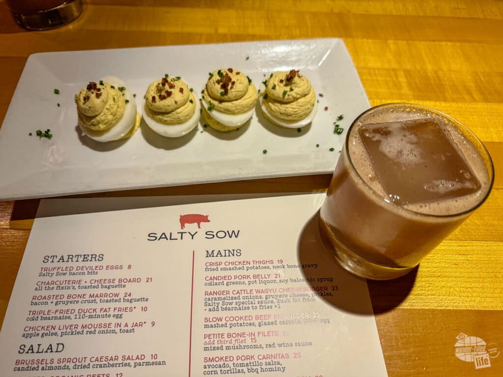 A plate filled with 4 deviled eggs. Next to the plate is a menu for the Salty Sow and a mixed drink.