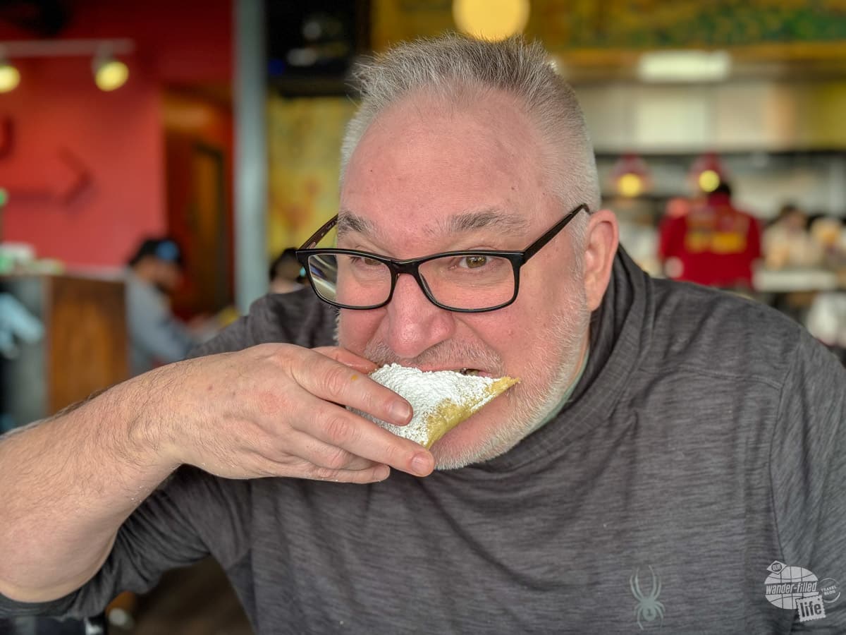 A man bites into a beignet topped with powdered sugar.