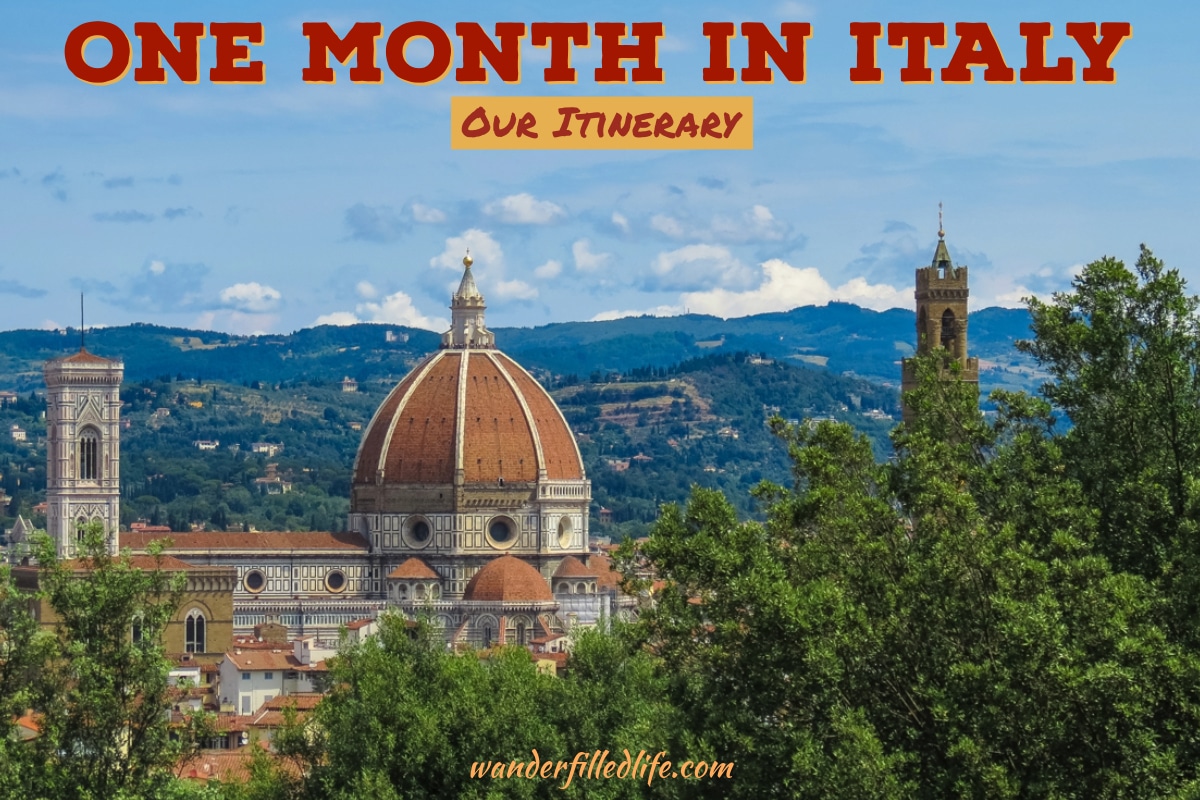Photo with text overlay. The photo shows the rounded dome of a cathedral along with a bell tower, with trees in the foreground and a hillside in the background. Text reads One Month in Italy: Our Itinerary.