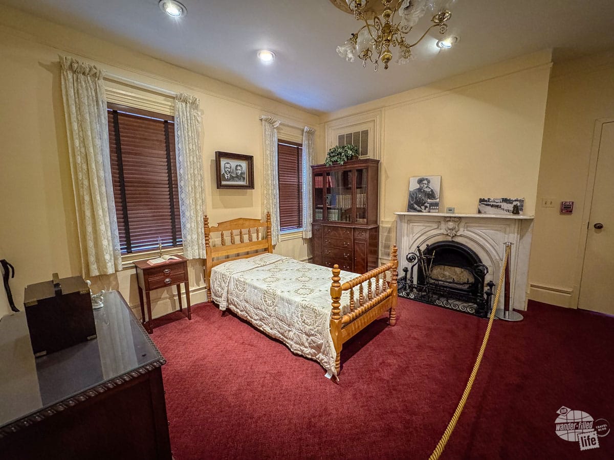 At the Mary McLeod Bethune Council House National Historic Site in Washington, DC. Photo shows a bedroom with a small twin bed, dresser, nightstand, bookshelf, and fireplace.