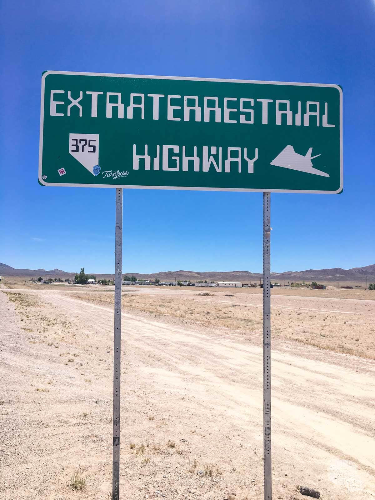 A green road sign in the midst of the desert labled the Extraterrestrial Highway in unusual script, with a silhouette of an Air Force Stealth Fighter on it.