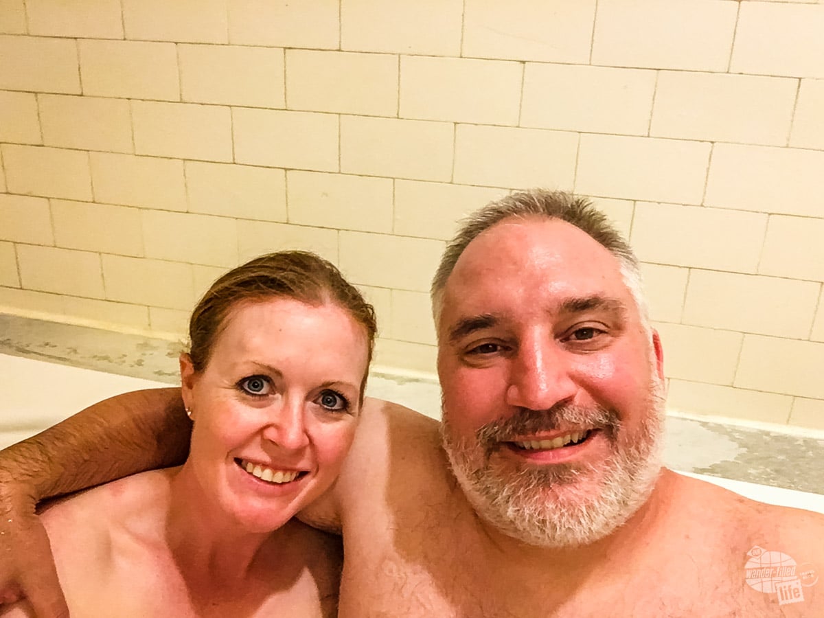 A man and a woman in a bath tub taking a selfie from the neck up.