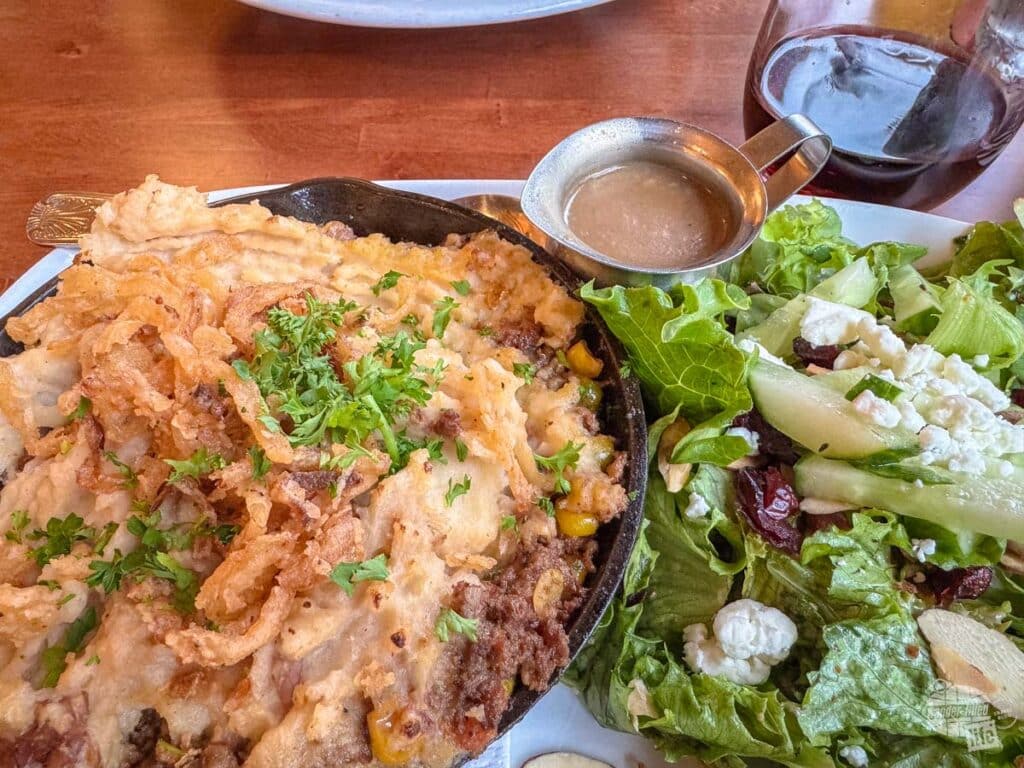 A small salad with salad dressing on the side of a large plate of shepherd's pie