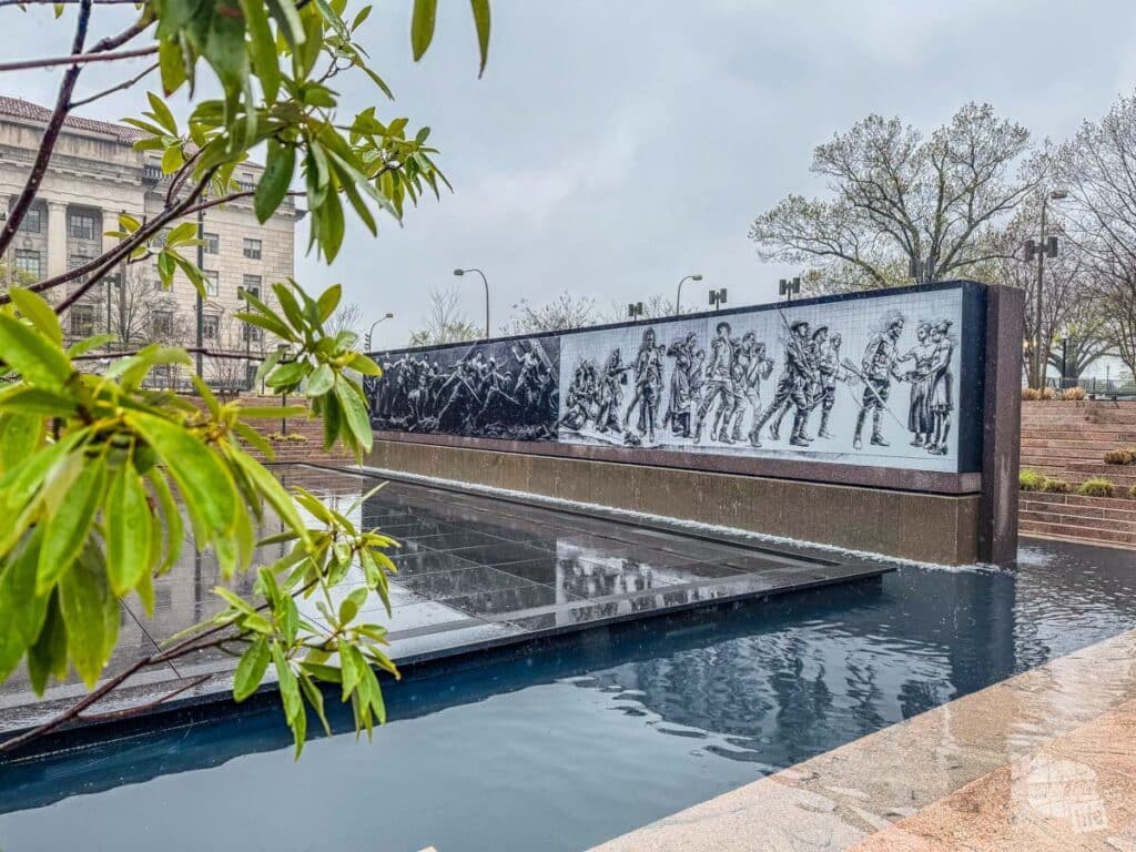 A low wall at the base of a pool with illustrations of soldiers carved into it.