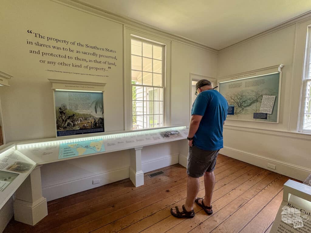 A man standing inside a room looking at an exhibit on the history of slavery on Snee Farm.