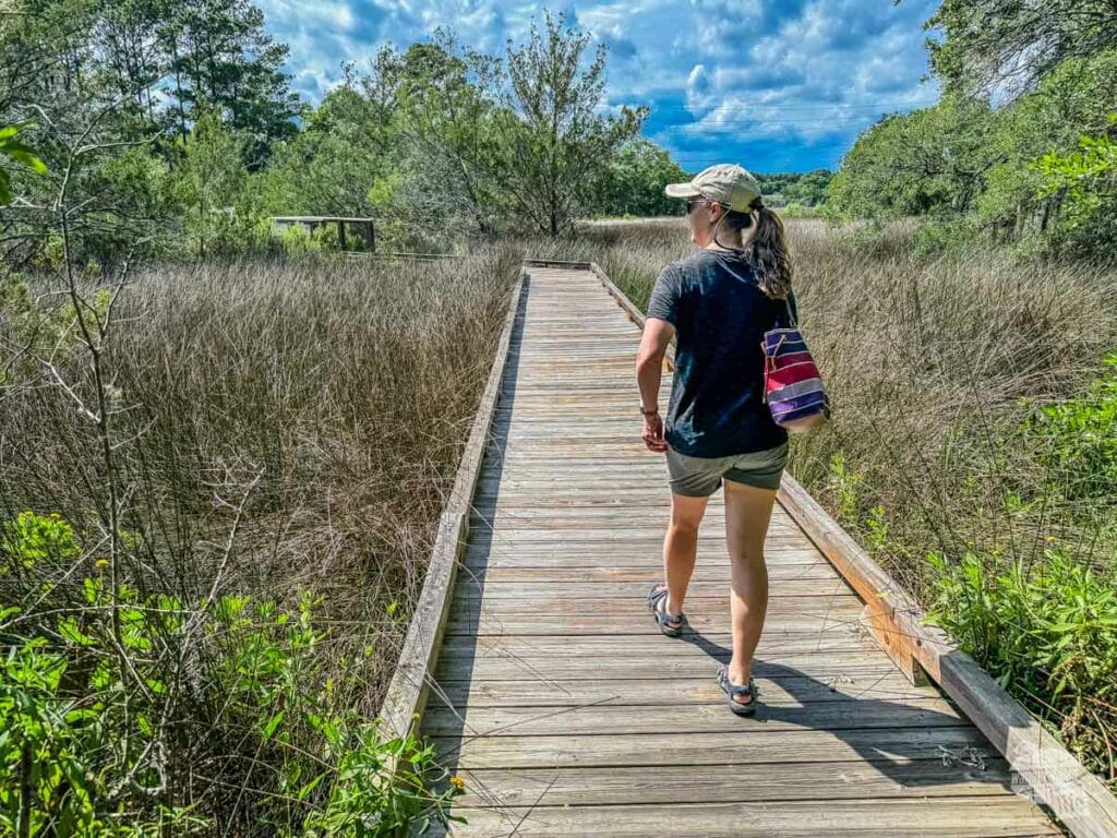 A woman walking a boardwalk out to a marsh.