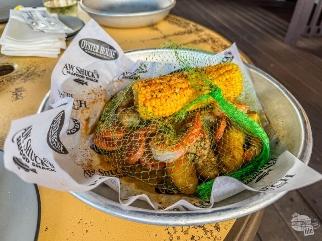 A plate with a mesh bag containing seasoned shrimp, potatoes, corn and sausage.