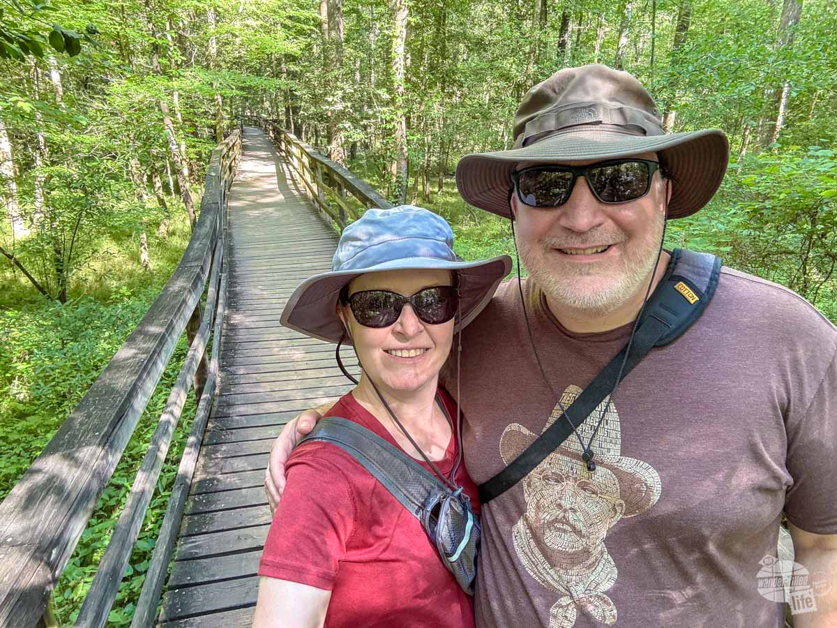 A man and a woman standing on a boardwalk trail through the trees.