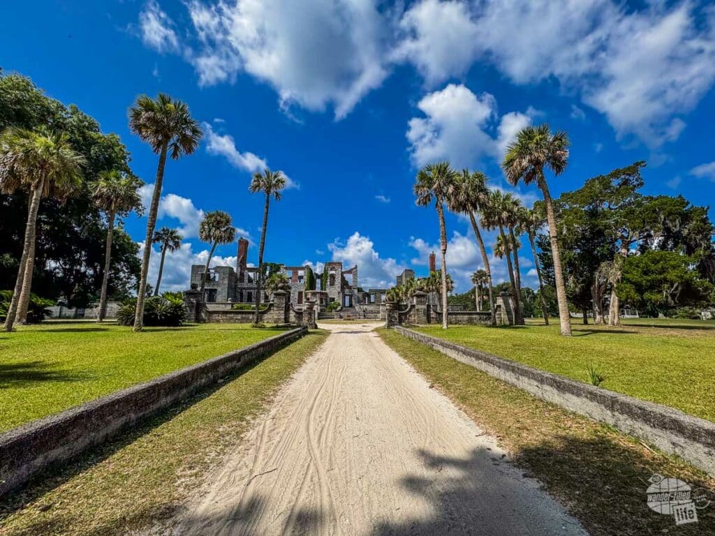 A sandy road leading to the ruins of a mansion.