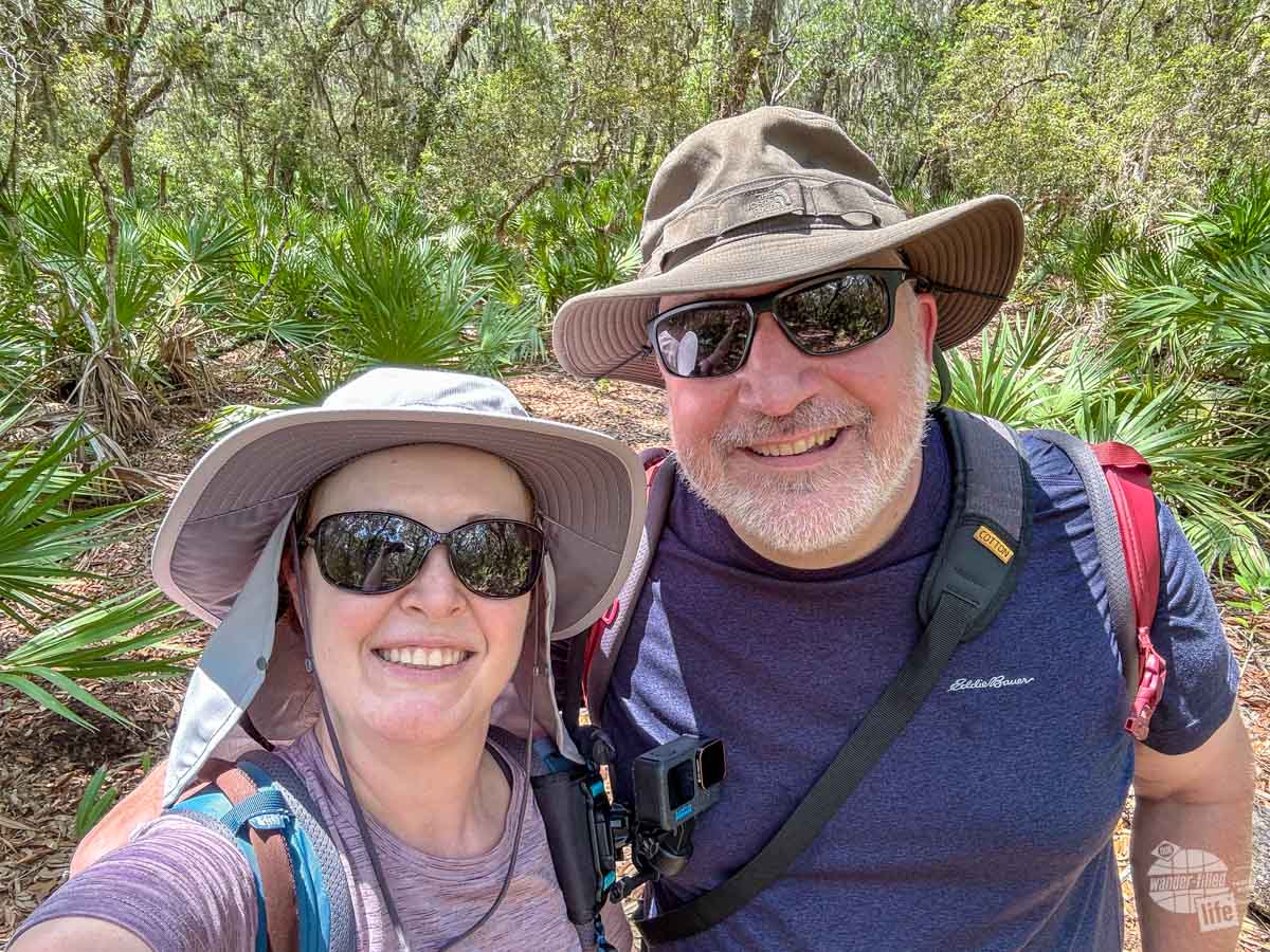 Grant and Bonnie taking a selfie on a trail. Both are wearing wide-brimmed hats, sunglasses and backpacks.