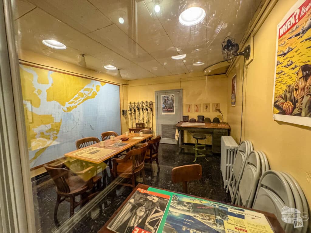 A World War II-era office with a map of Charleston Harbor on the wall. There are serveral desks and radios.