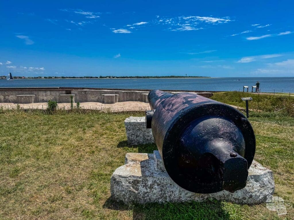 A cannon on a grassy slope looking out over Charleston Harbor at the coast.