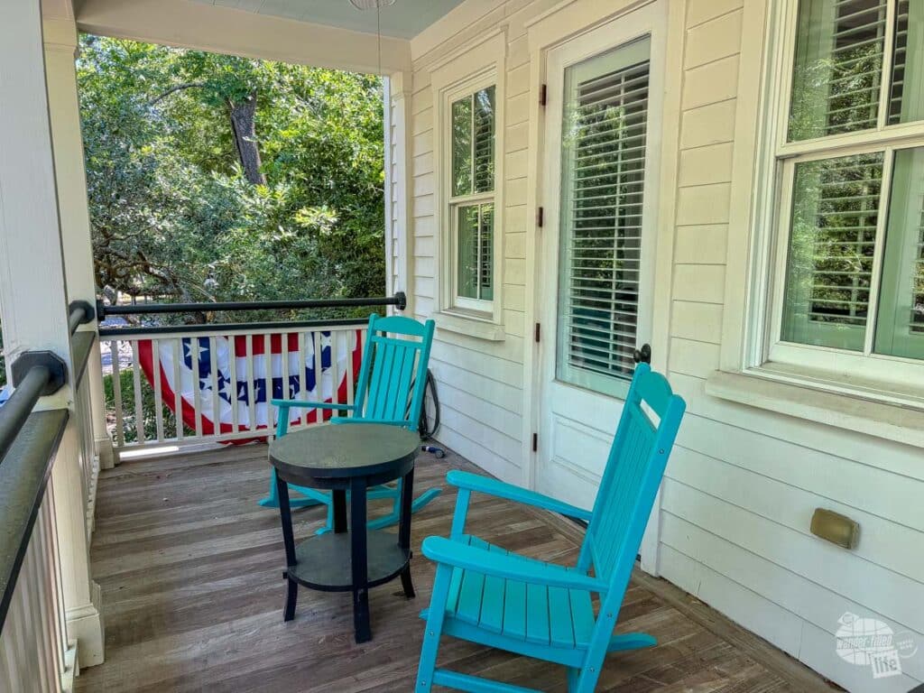 A pair of rocking chairs with a small table on a balcony with a white building behind them.